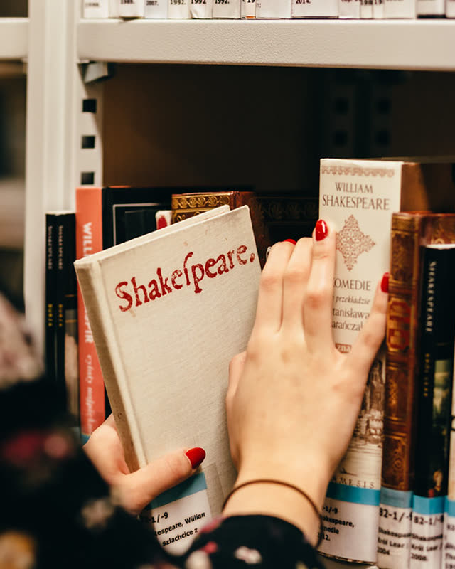 Hand zieht ein Shakespeare-Buch aus einem Bibliotheksregal